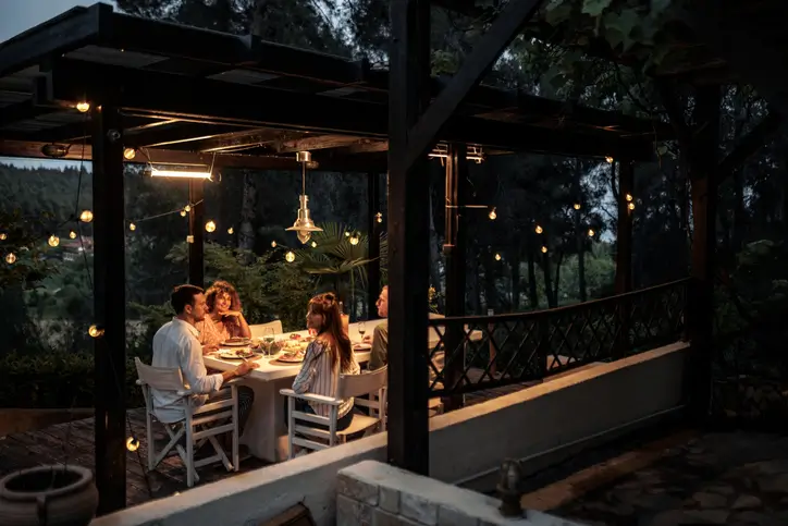 Friends eating dinner on their wooden deck under outdoor string lights