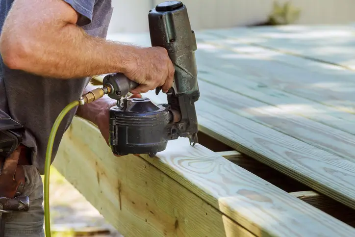 Patio construction man using pneumatic gun to install wood on deck